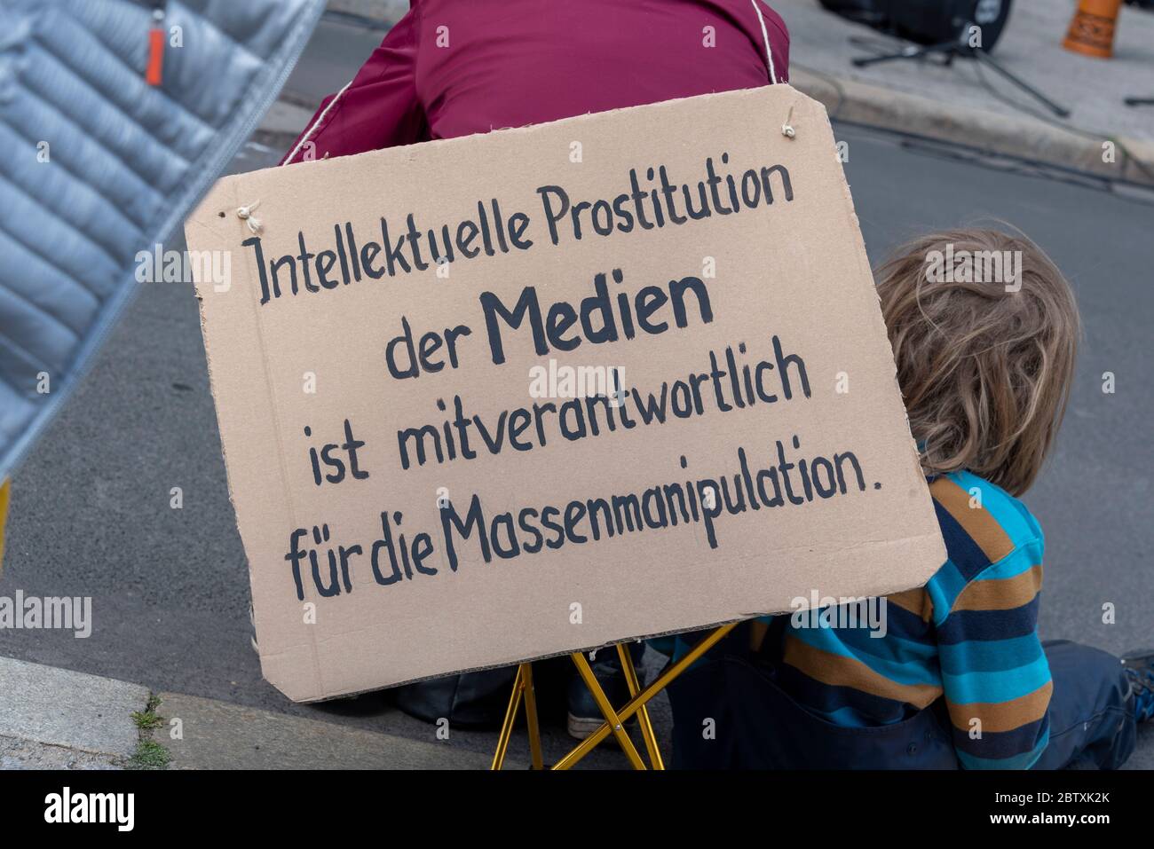 Magdeburg, Germany. 16th May, 2020. A woman is sitting with her child in the Old Market Square. On her back is a sign saying: 'Intellectual prostitution by the media is partly responsible for the mass manipulation.' In the state capital on Saturday people demonstrated on the Alter Markt against the Corona restrictions. Similar demos are taking place nationwide. Critics fear that the protests will be appropriated by right-wing groups. Credit: Stephan Schulz/dpa-Zentralbild/ZB/dpa/Alamy Live News Stock Photo