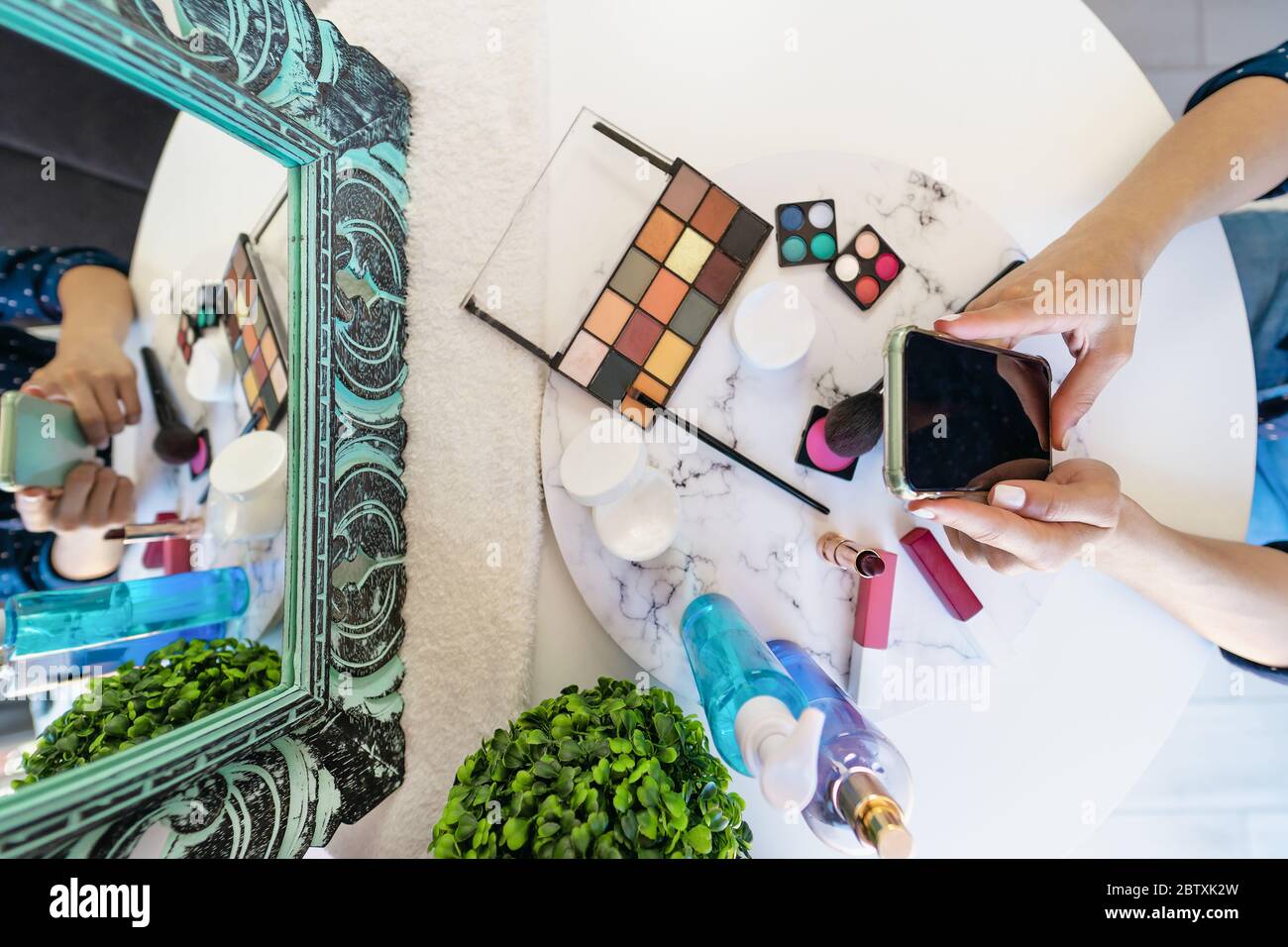 Top view young woman using mobile smartphone while doing makeup at home - Beauty cosmetic industry and technology addicted people concept Stock Photo