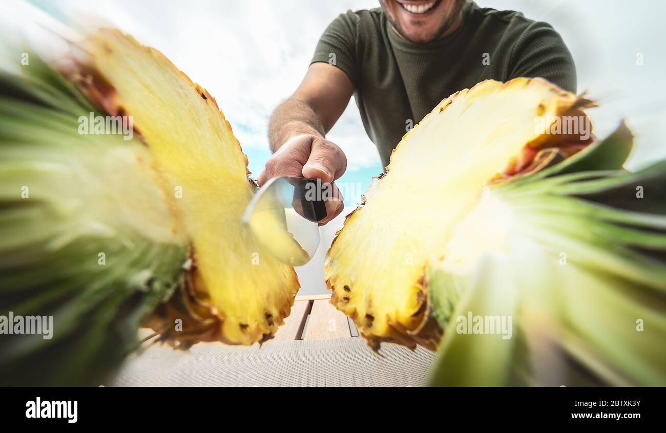 Young smiling man cutting pineapple - Close up male hand holding sharp knife preparing tropical fresh fruits Stock Photo