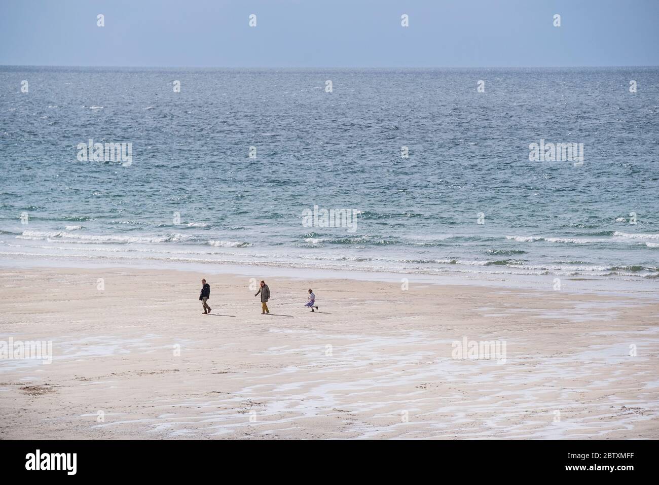 Due to the Coronavirus Covid 19 pandemic the normally busy Fistral Beach is now empty except for three people walking along the shoreline in Newquay i Stock Photo