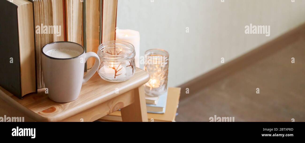 Self isolation, stay home, hygge and cozy home concept - books, cup of coffee or hot chocolate and candles, seasonal autumn fall winter relax time, co Stock Photo