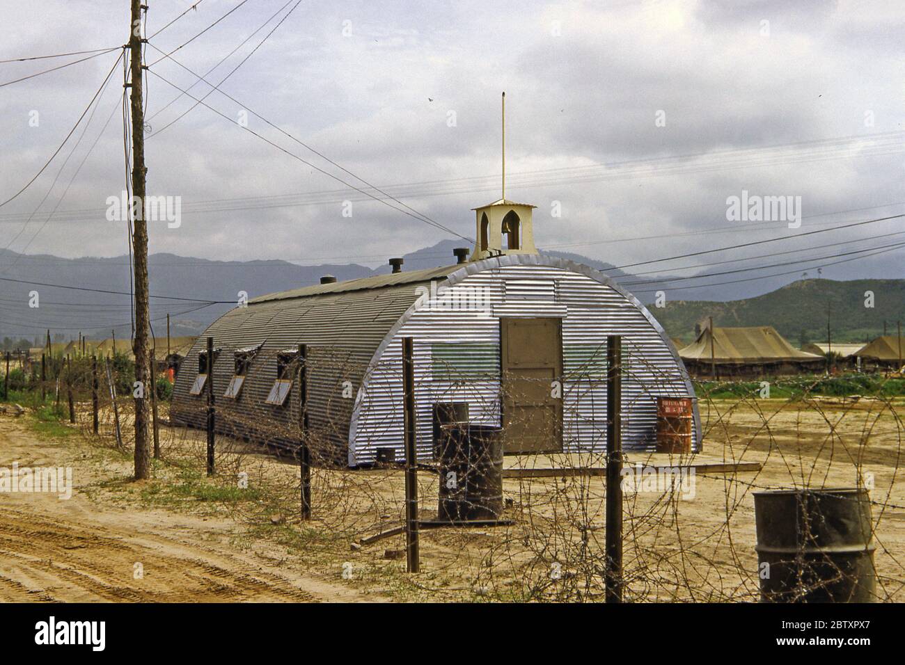 A meeting building/church made from a Quonset hut for the US Army's 40th Infantry, Division Replacement Company during the Korean War campaign, South Korea, 1953. A Quonset hut is a lightweight prefabricated structure of corrugated galvanized steel having a semi-circular cross-section. The design was developed in the United States, based on the Nissen hut first made by the British during World War I. Hundreds of thousands were produced during World War II. The name comes from the site of their first manufacture at Quonset Point, Davisville, Rhode Island. Stock Photo