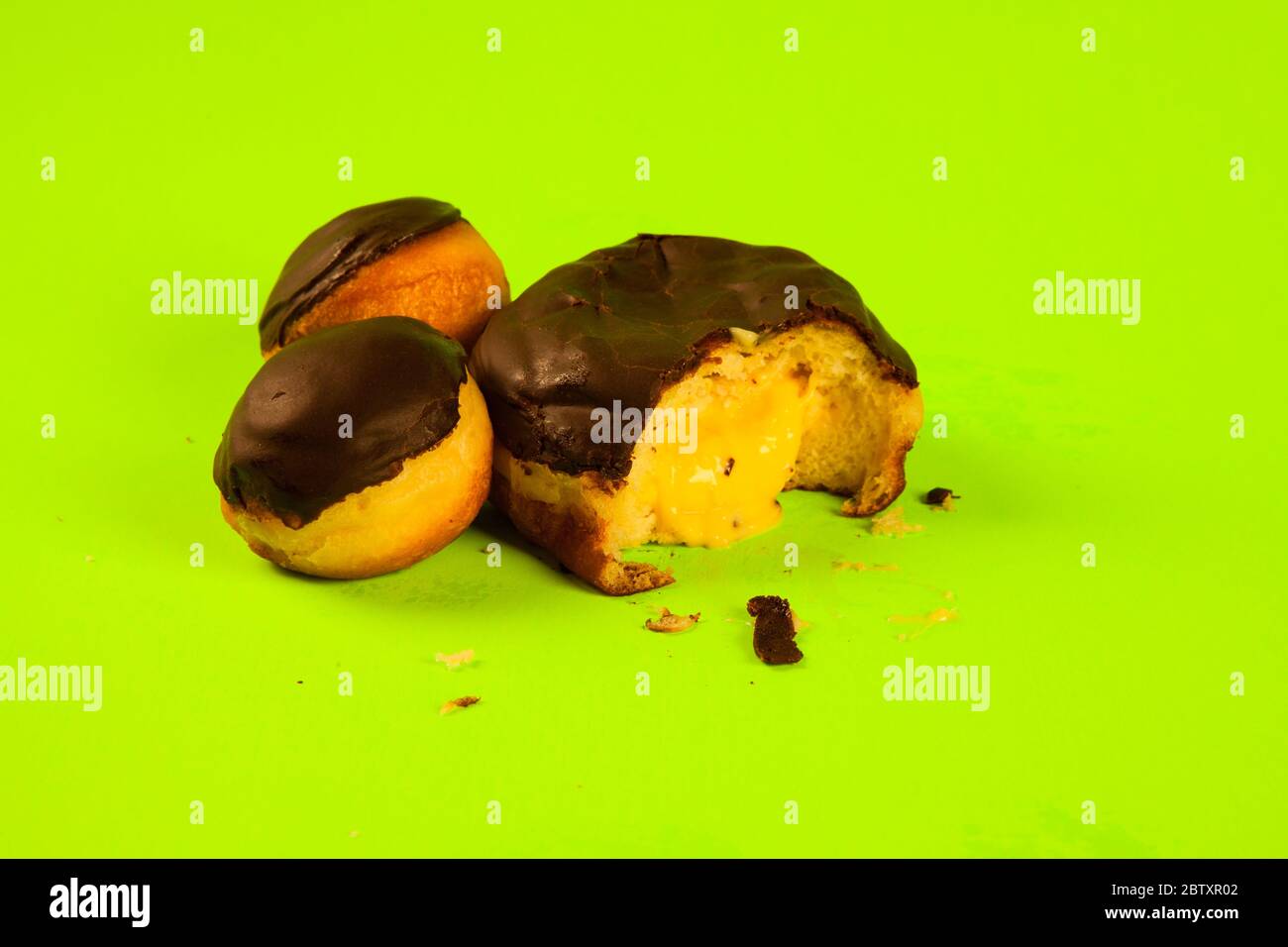 Boston cream donut large and small on green background oosing with custard Stock Photo
