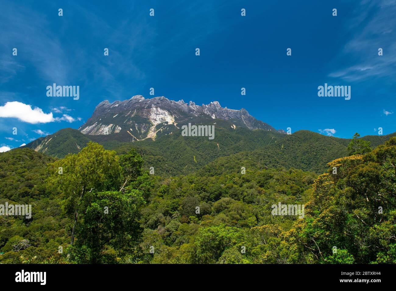 Summit and peaks of Mount Kinabalu in sunlight, with beautiful rainforest in the foreground, and sky above. Mount Kinabalu, Sabah, Borneo, Malaysia Stock Photo