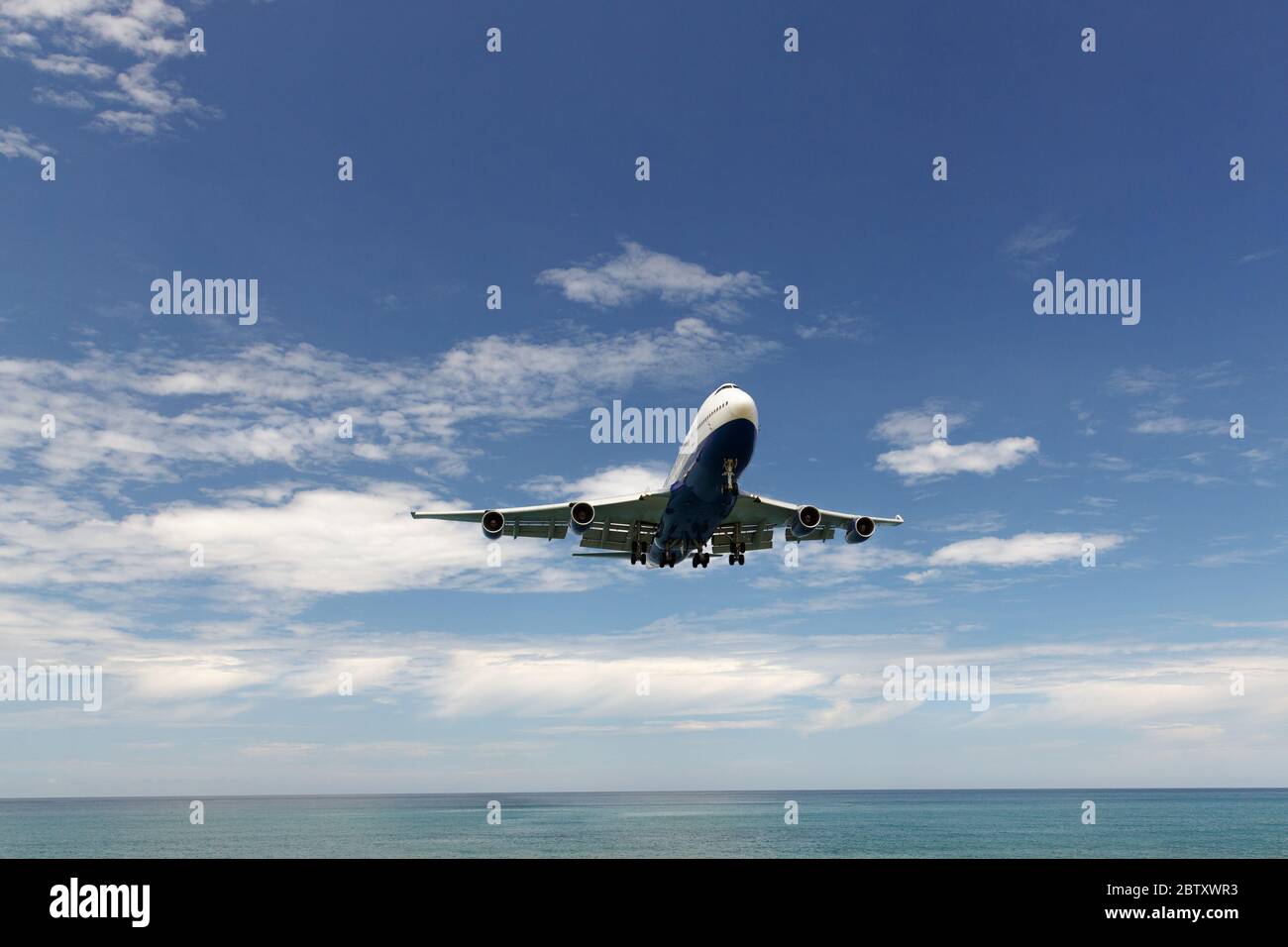 Vacation, travel, aviation concept. Modern commercial airplane jetliner flying in blue sky above the sea, copy space. Bottom view. Stock Photo