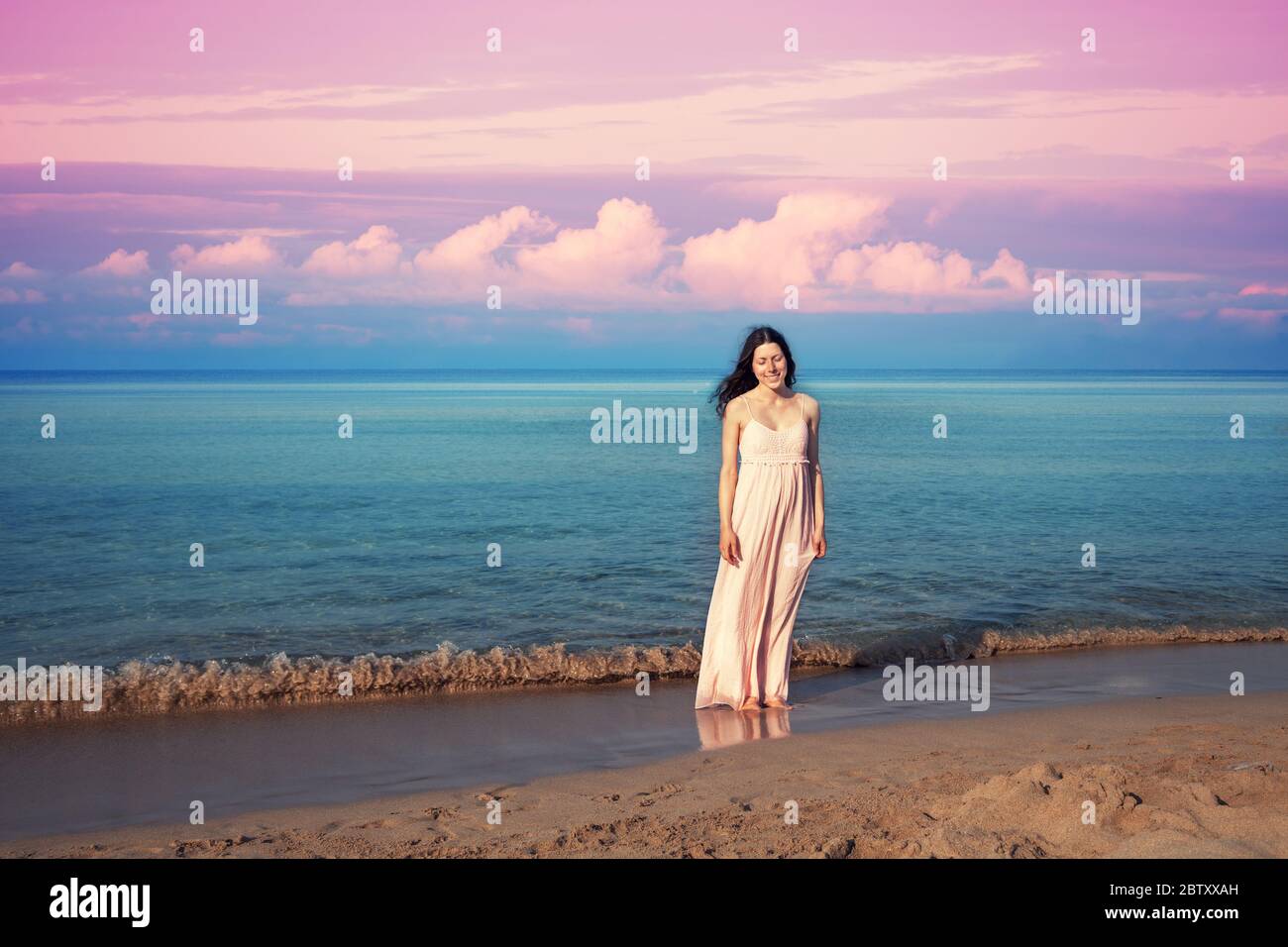 Young happy woman in a long dress on the beach at sunrise. Summertime Stock Photo