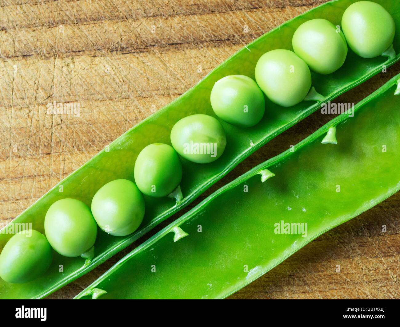 Fresh garden peas in an open pod on a wooden chopping board Stock Photo