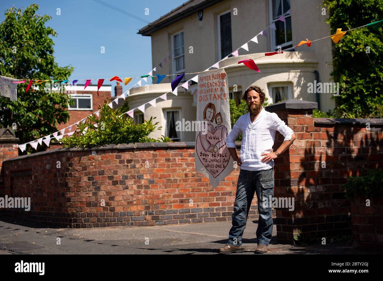 Artist Luke Perry on Duncombe Street in Wollaston, where he has hung bunting with messages of support for neighbours and key workers, to create a 500 metre corridor of colour through the West Midlands village. Mr Perry asked local residents and shopkeepers to submit designs and messages, which he then hand painted and stitched onto bunting with the help of volunteers. Stock Photo
