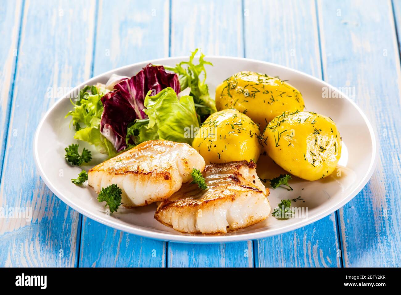 Fried fish with potatoes and vegetable salad on wooden table Stock Photo