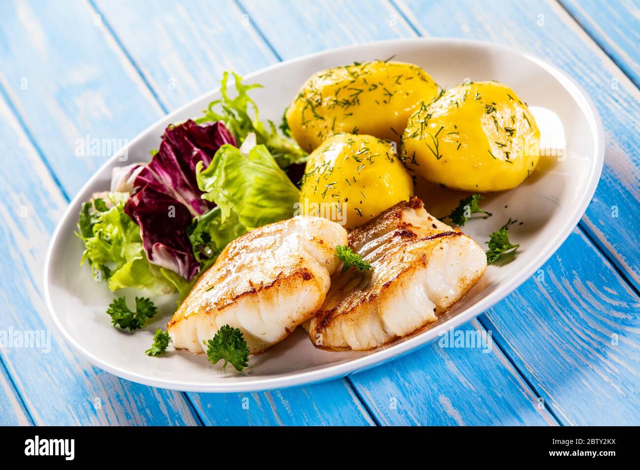 Fried fish with potatoes and vegetable salad on wooden table Stock Photo