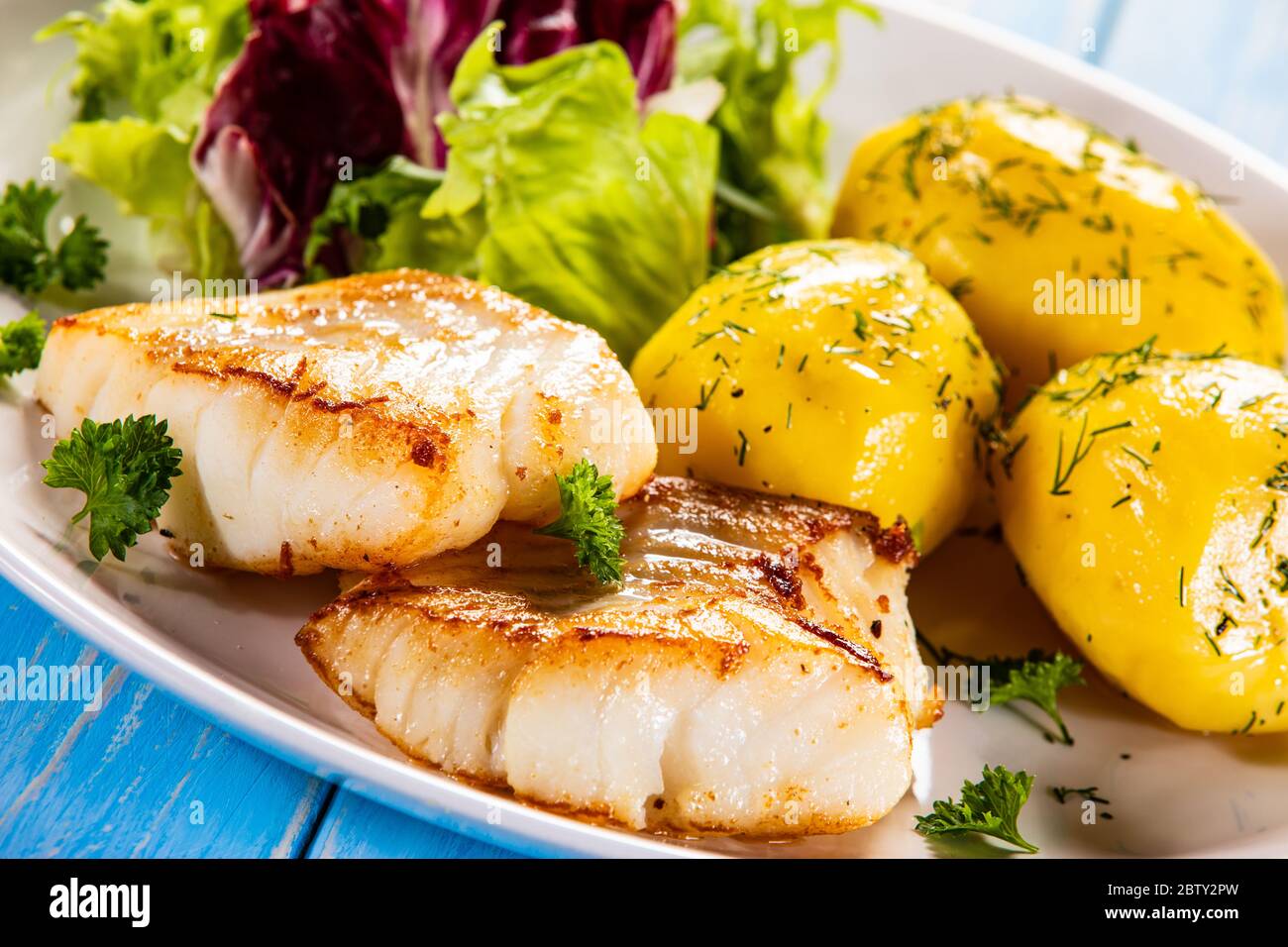 Fried fish with potatoes and vegetable salad on wooden table Stock Photo