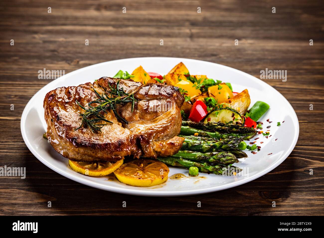 Grilled steak with asparagus and grilled vegetables on wooden table Stock Photo