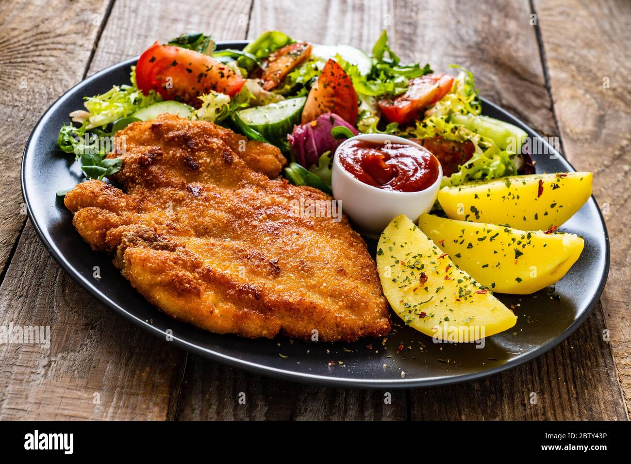 Schnitzel with boiled potatoes and vegetable salad on wooden background Stock Photo