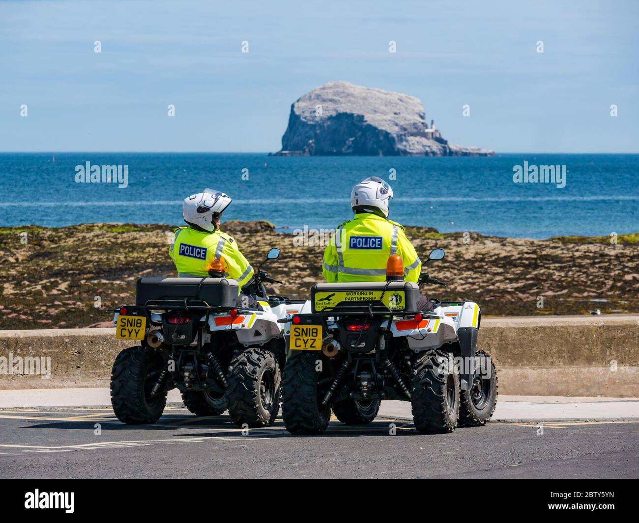 North Berwick, East Lothian, Scotland, United Kingdom, 28th May 2020. Easing of lockdown restrictions: with the Scottish Government set to announce the lifting of some lockdown restrictions today, there are already signs that things are beginning to return to normal in the popular seaside town. Police on quad bikes patrol the beach during lockdown and pause for a rest stop in Milsey Bay with the bass Rock gannet colony on the horizon on a sunny day Stock Photo