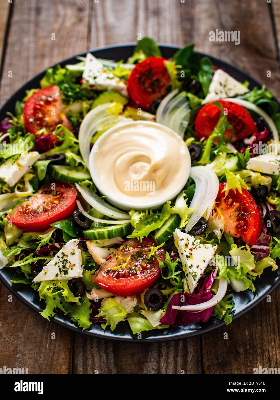 Greek salad with sauce on wooden background Stock Photo