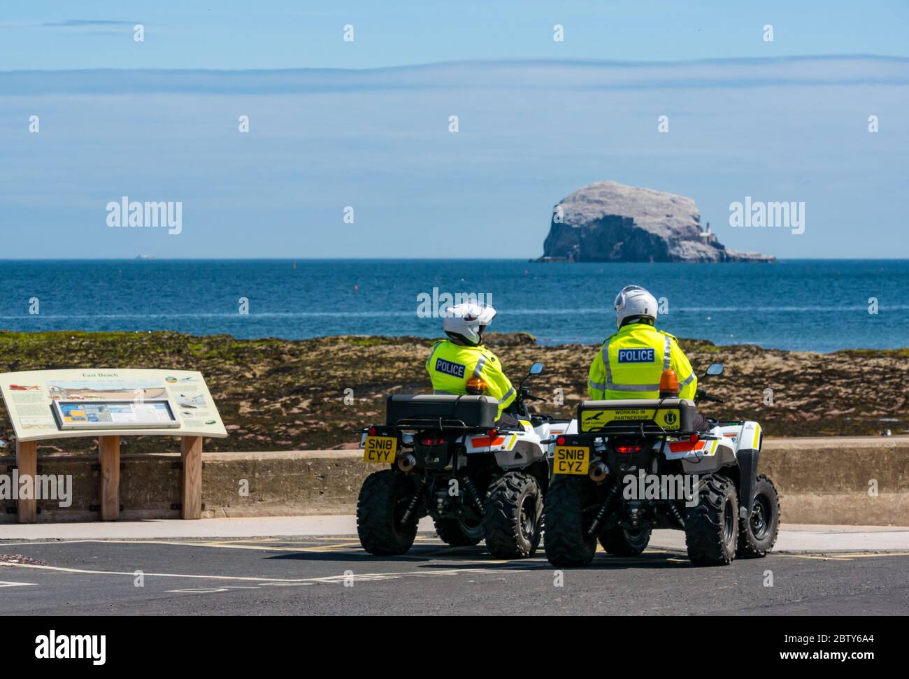 North Berwick, East Lothian, Scotland, United Kingdom, 28th May 2020. Easing of lockdown restrictions: with the Scottish Government set to announce the lifting of some lockdown restrictions today, there are already signs that things are beginning to return to normal in the popular seaside town. Police on quad bikes patrol the beach during lockdown and pause for a rest stop in Milsey Bay with the Bass Rock gannet colony on the horizon on a sunny day Stock Photo