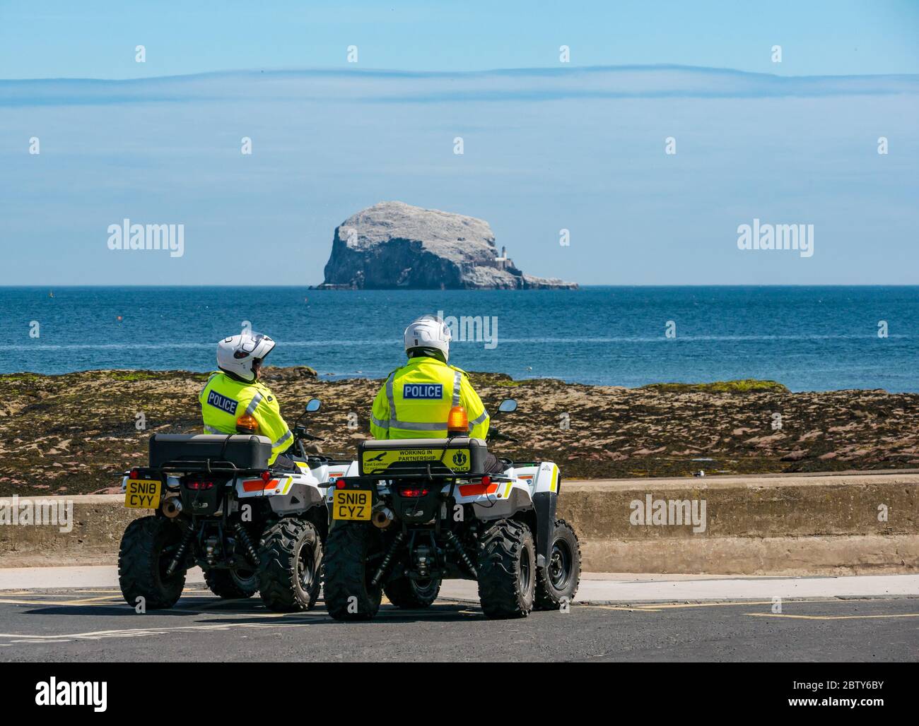 North Berwick, East Lothian, Scotland, United Kingdom, 28th May 2020. Easing of lockdown restrictions: with the Scottish Government set to announce the lifting of some lockdown restrictions today, there are already signs that things are beginning to return to normal in the popular seaside town. Police on quad bikes patrol the beach during lockdown and pause for a rest stop in Milsey Bay with the bass Rock gannet colony on the horizon on a sunny day Stock Photo