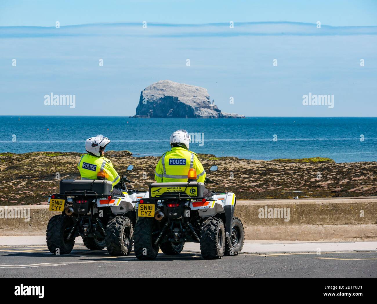 North Berwick, East Lothian, Scotland, United Kingdom, 28th May 2020. Easing of lockdown restrictions: with the Scottish Government set to announce the lifting of some lockdown restrictions today, there are already signs that things are beginning to return to normal in the popular seaside town. Police on quad bikes patrol the beach during lockdown and pause for a rest stop in Milsey Bay with the bass Rock gannet colony on the horizon on a sunny day Stock Photo