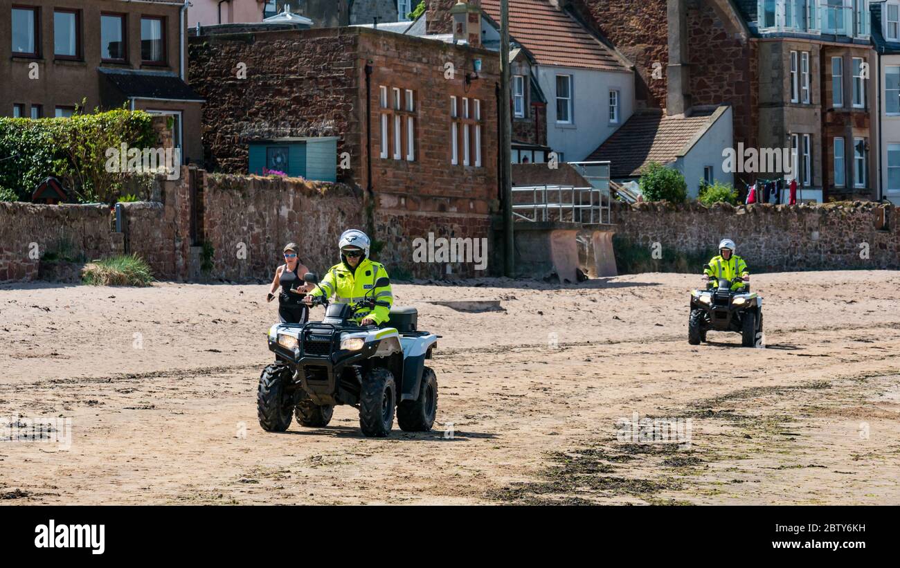 North Berwick, East Lothian, Scotland, United Kingdom, 28th May 2020. Easing of lockdown restrictions: with the Scottish Government set to announce the lifting of some lockdown restrictions today, there are already signs that things are beginning to return to normal in the popular seaside town. Police on quad bikes patrol the beach during the Covid-19 pandemic lockdown as a woman jogs in the beach Stock Photo