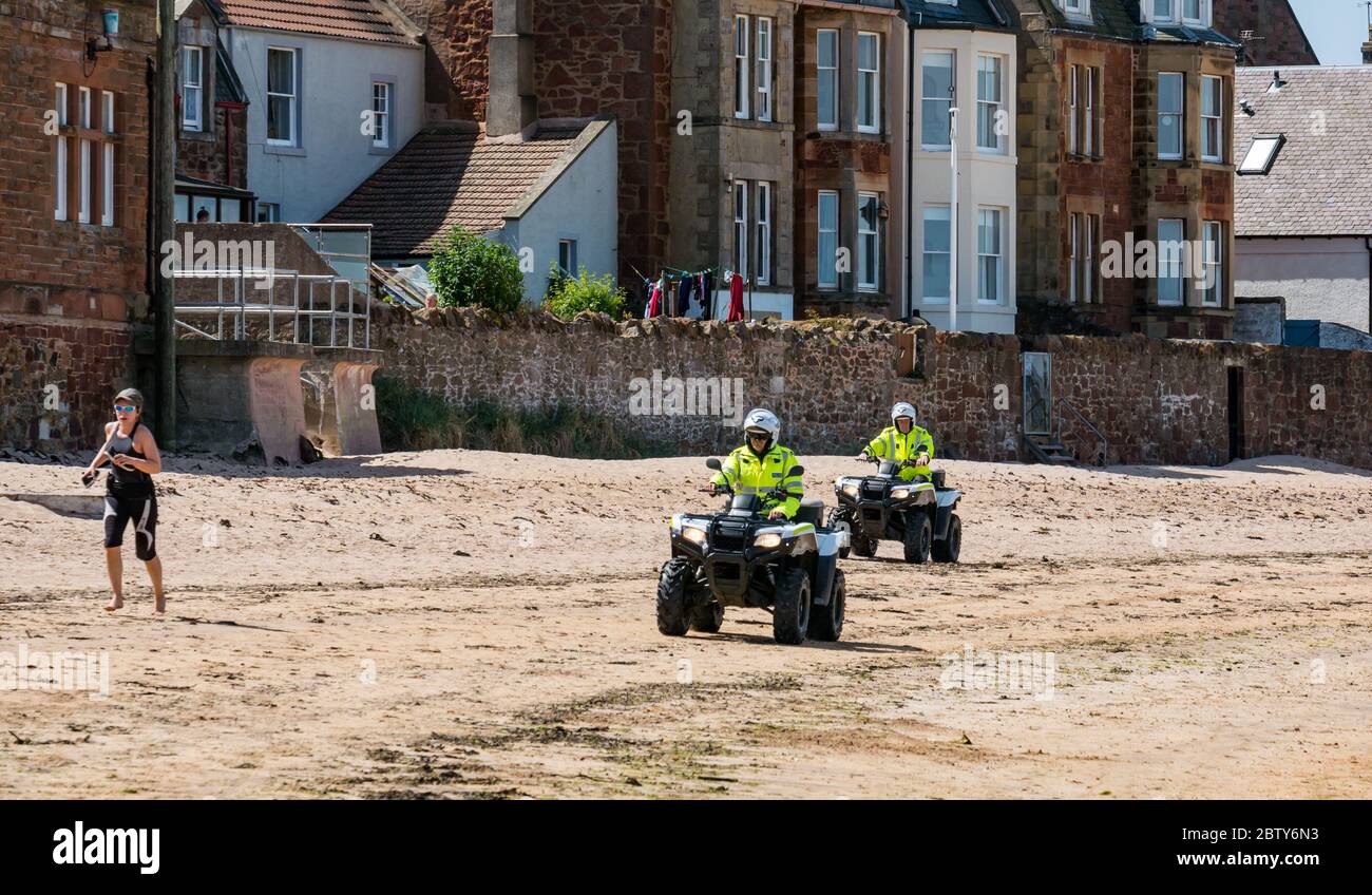 North Berwick, East Lothian, Scotland, United Kingdom, 28th May 2020. Easing of lockdown restrictions: with the Scottish Government set to announce the lifting of some lockdown restrictions today, there are already signs that things are beginning to return to normal in the popular seaside town. Police on quad bikes patrol the beach during the Covid-19 pandemic lockdown as a woman jogs in the beach Stock Photo