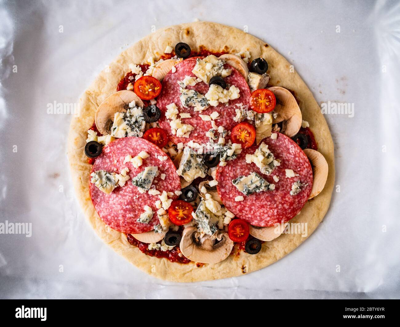 Unbaked pizza with salami, champignon,olives and cherry tomatoes Stock Photo