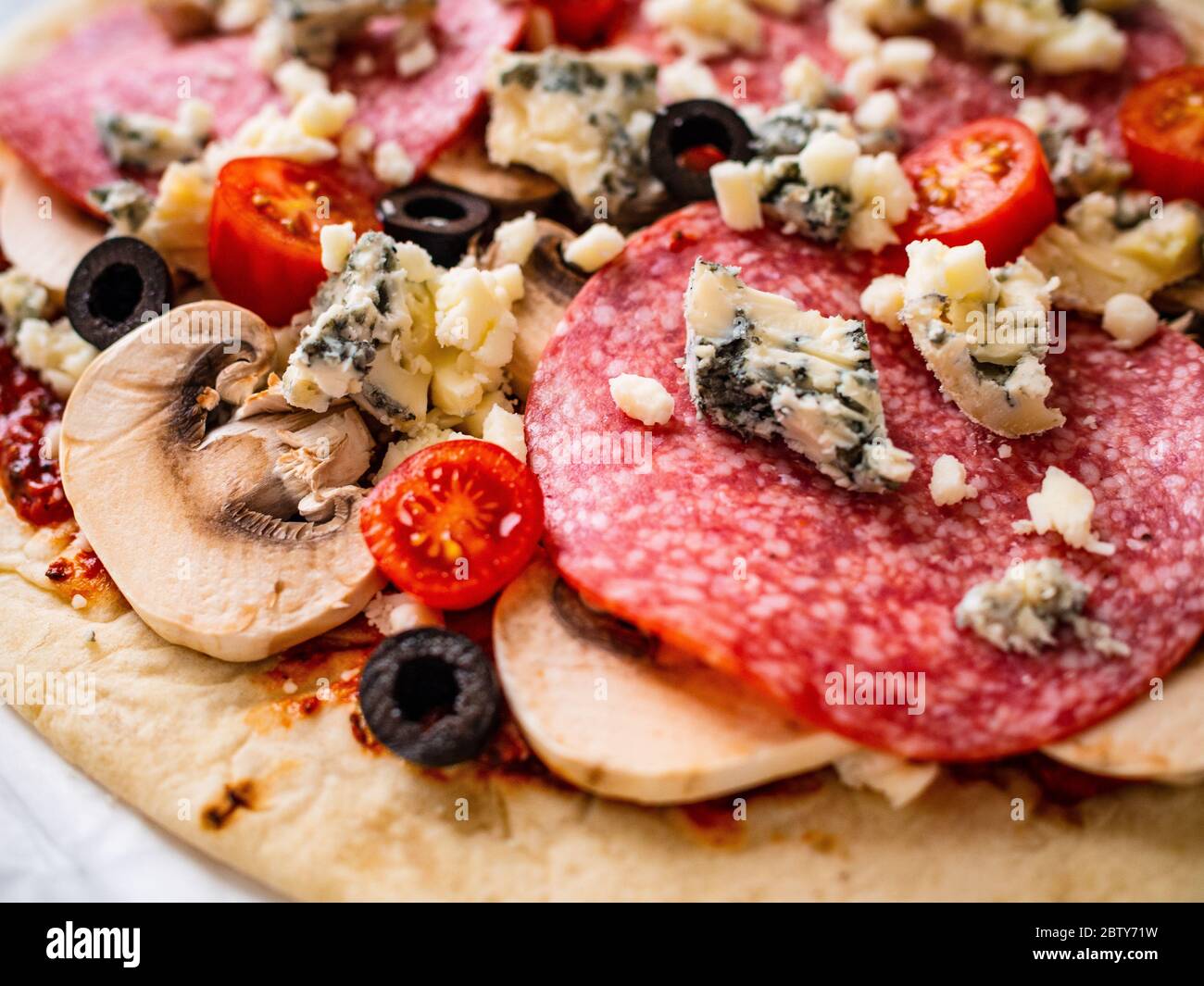 Unbaked pizza with salami, champignon,olives and cherry tomatoes Stock Photo