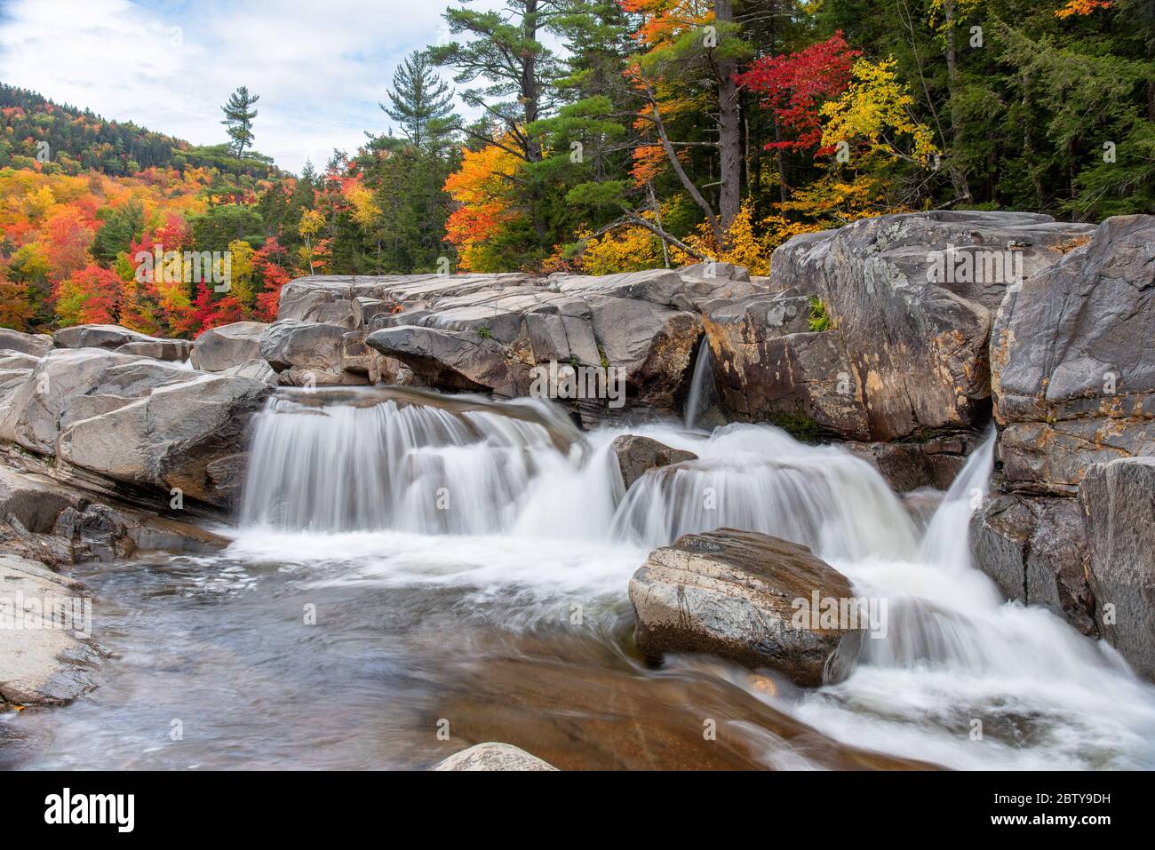 Waterfall along a mountain river on a cloudy autumn morning. Stunning autumn colours in background. Stock Photo