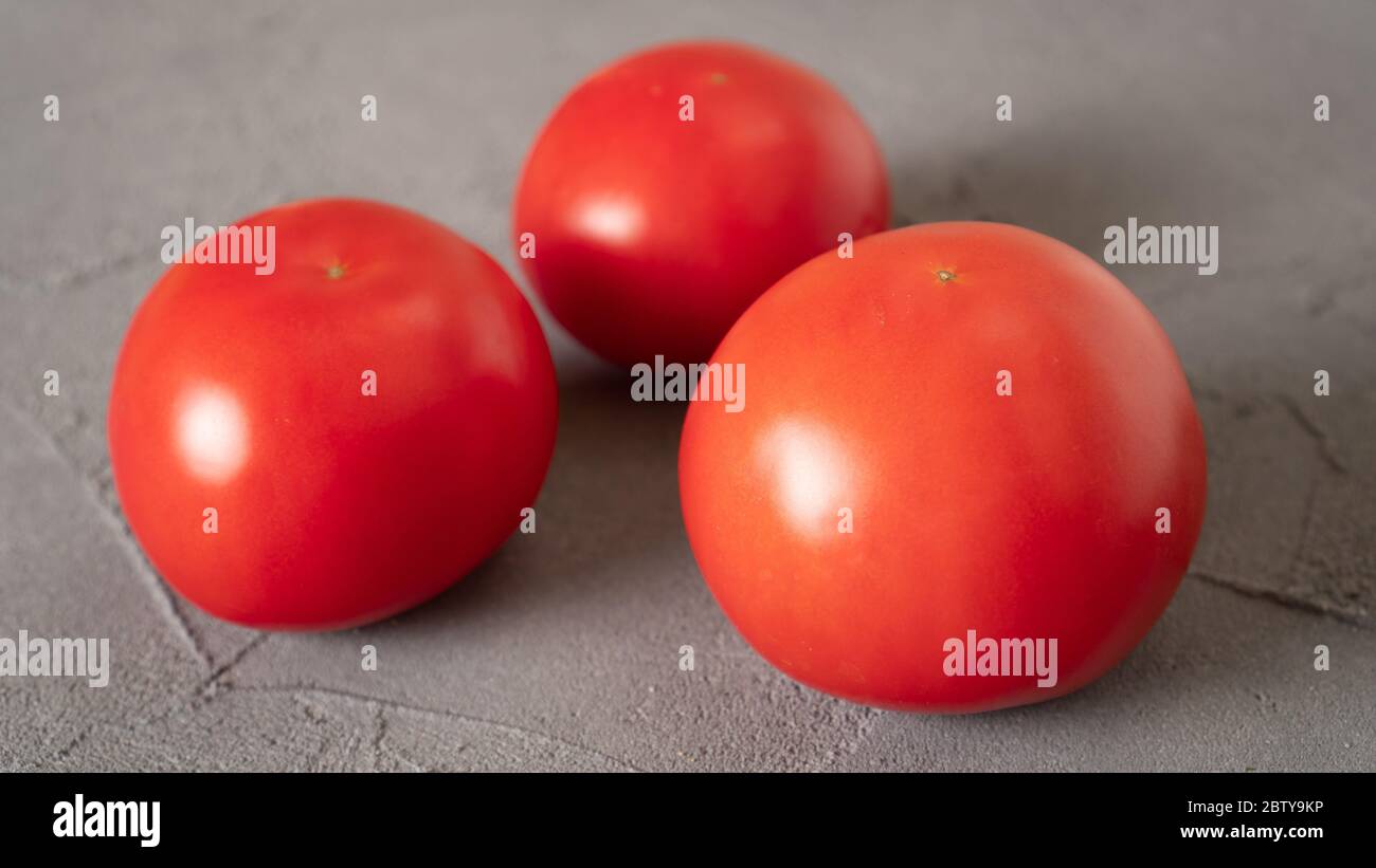 Close up three isolated tomatoes on concrete background. Fresh and healthy food good for your eyes, heart and kidneys. Stock Photo
