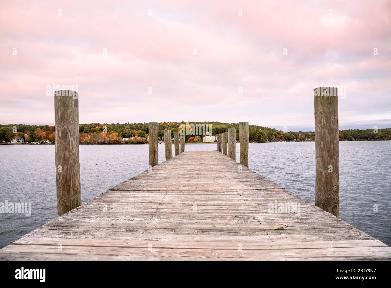Deserted wooden jetty on a lake at dusk. Beautiful fall foliage visible on the other side of the lake. Concept of tranquility. Stock Photo