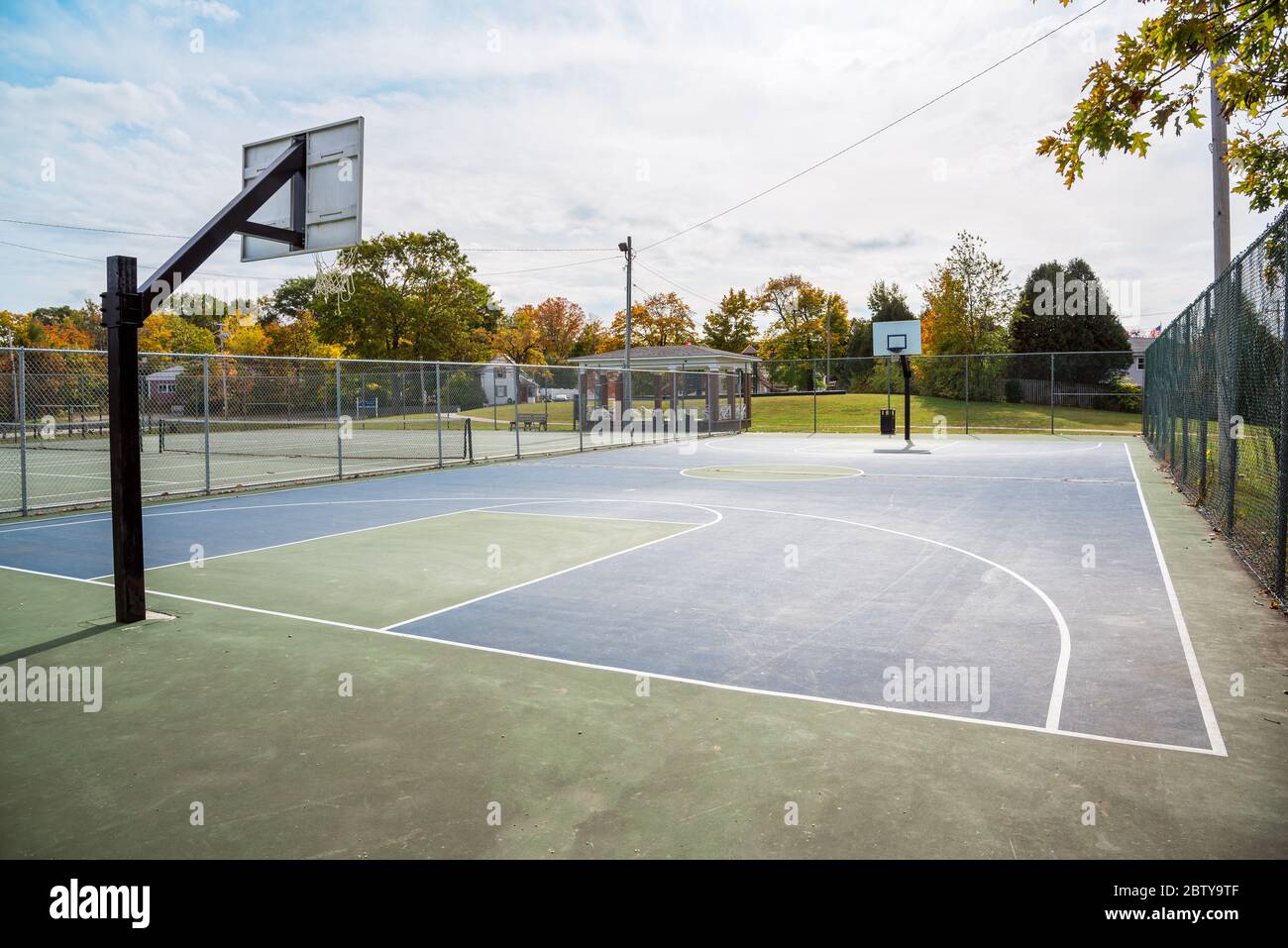 View of a deserted fenced basketball court in a public park on a sunny autumn morning Stock Photo