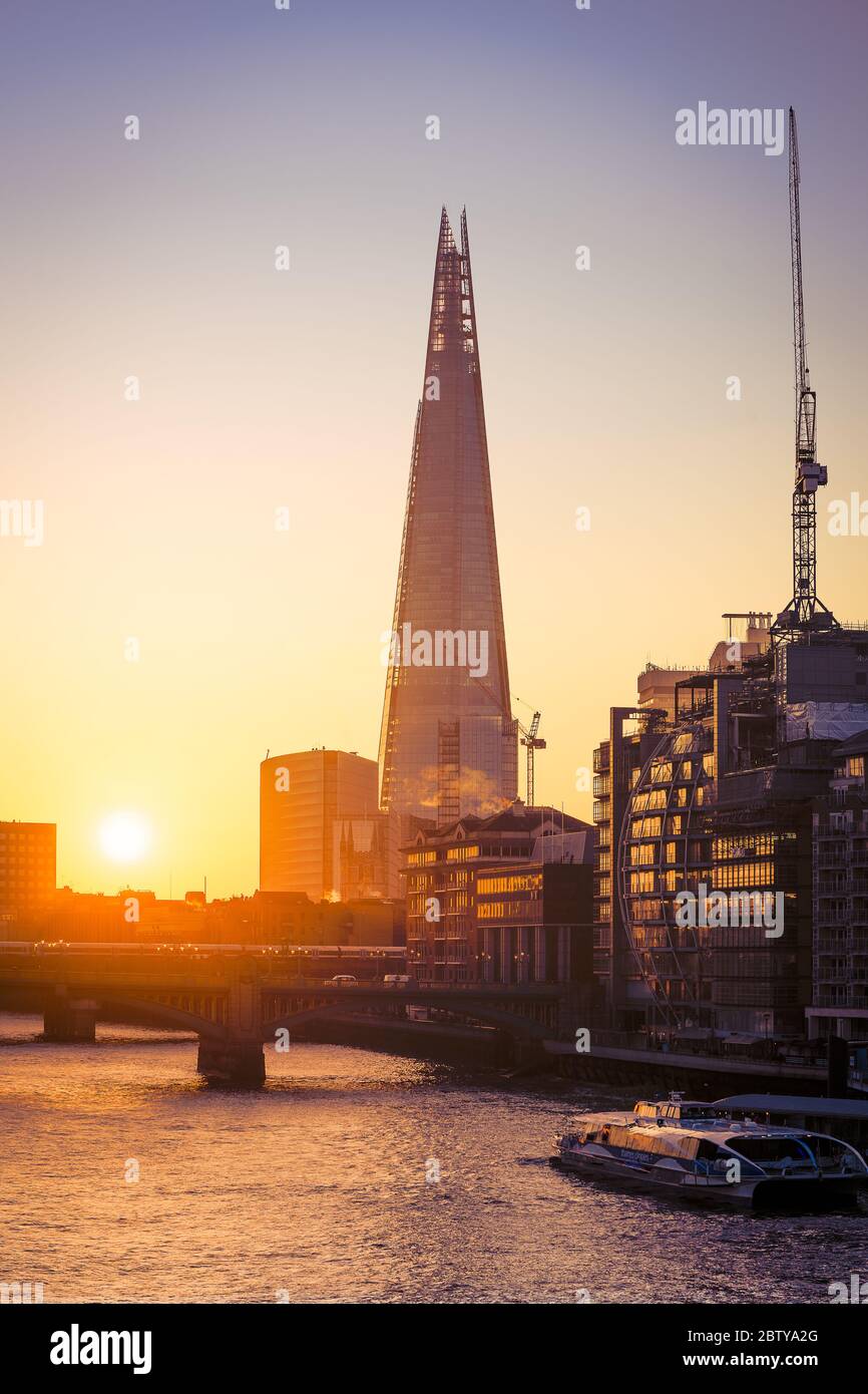 The Shard at sunrise on a cold winters morning with River Thames and river cruise boat and sun reflections in windows, London, England, United Kingdom Stock Photo