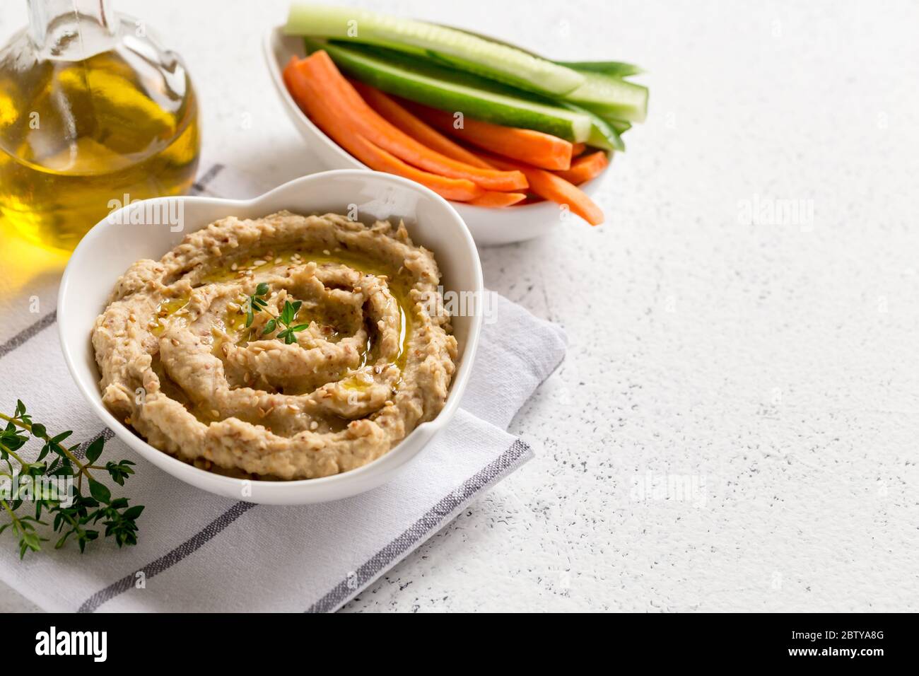 hummus sauce in a bowl, sesame seeds, olive oil, cucumber and carrots on a light background Stock Photo