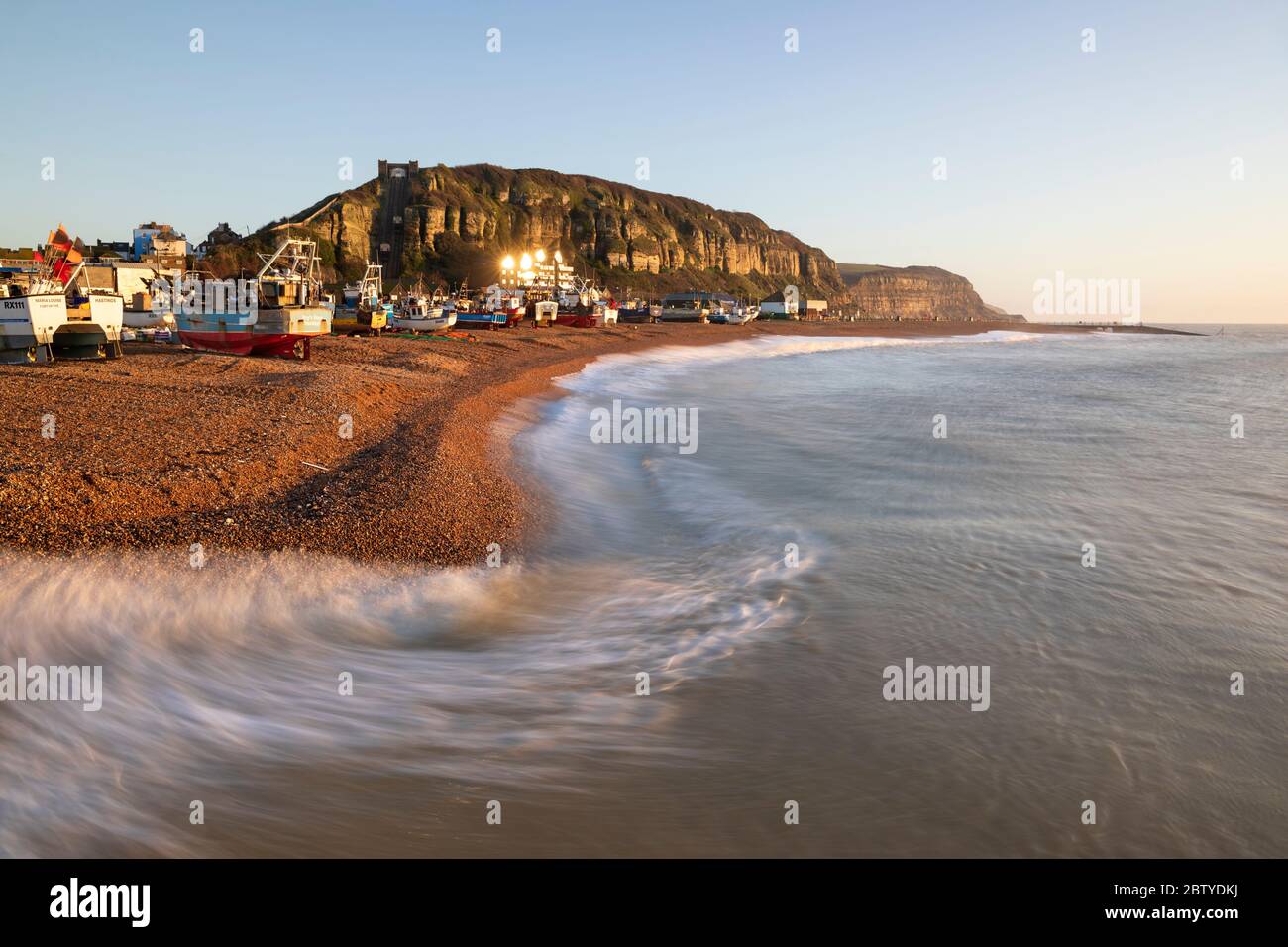 Fishing boats on beach at The Stade with breaking waves and East Hill behind at sunrise, Hastings, East Sussex, England, United Kingdom, Europe Stock Photo