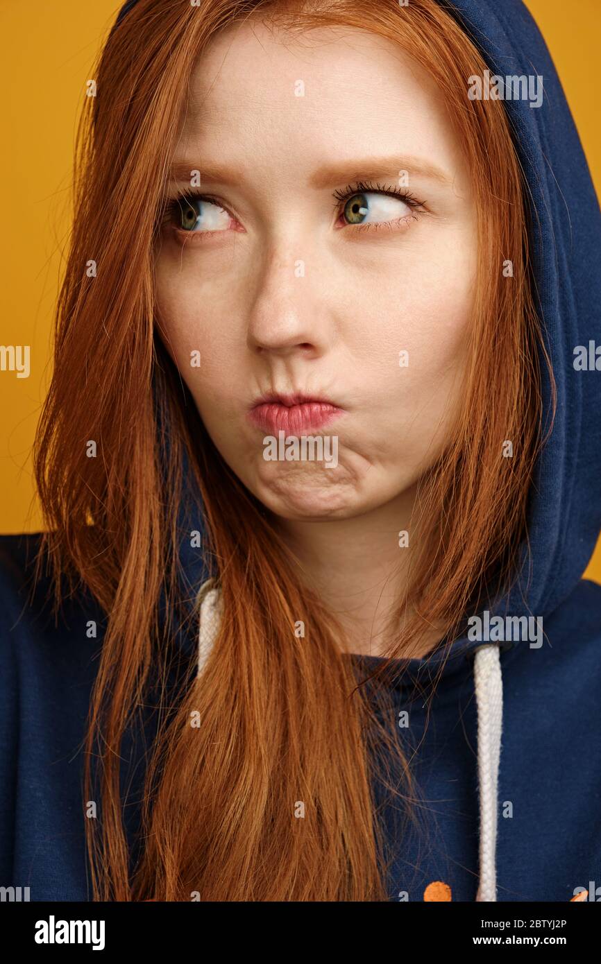 Head shot. Redhaired girl in a blue hood looks displeased to the side