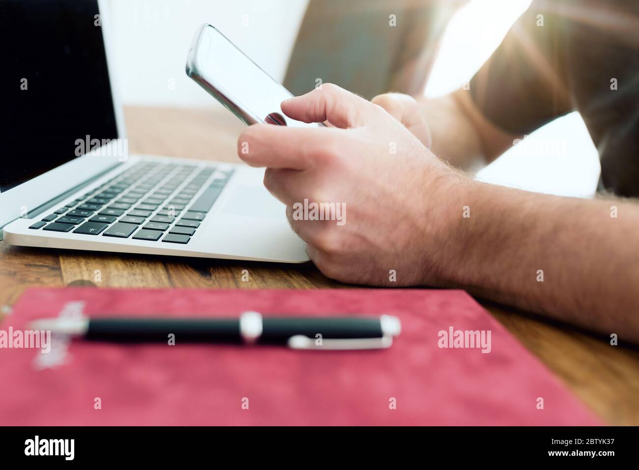 close-up of man using smartphone in front of laptop computer in home office Stock Photo