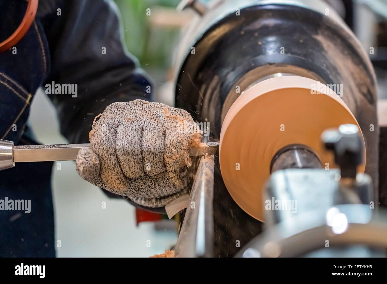 Carpenter man is shaving surface of the wooden bowl. Spinning wood wheel. Carving outside forming a round detail. Joiner is using metal tool to make t Stock Photo