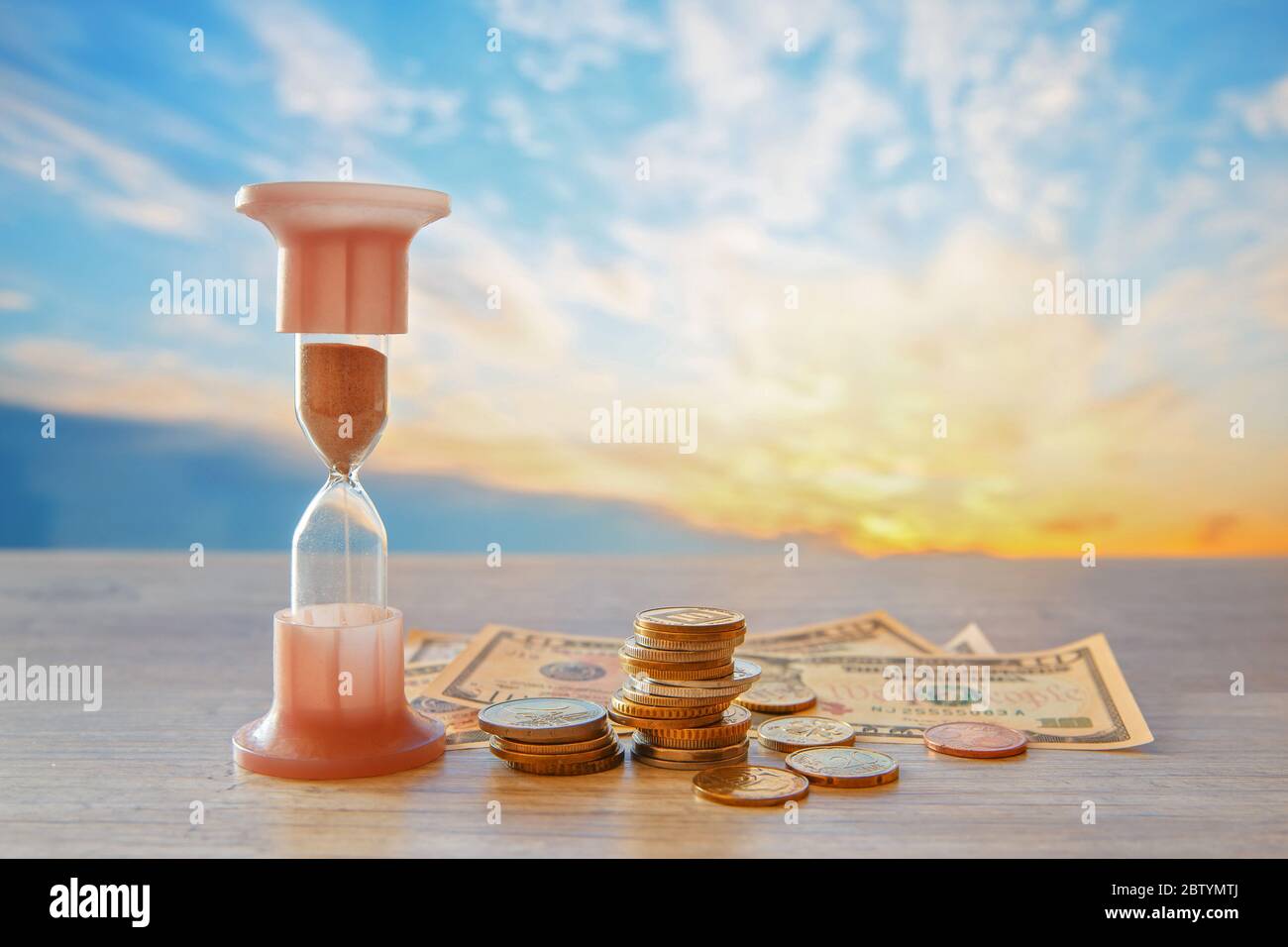 Time is money. Financial concept of money with a clock and coins of different countries. Hourglass. Stock Photo