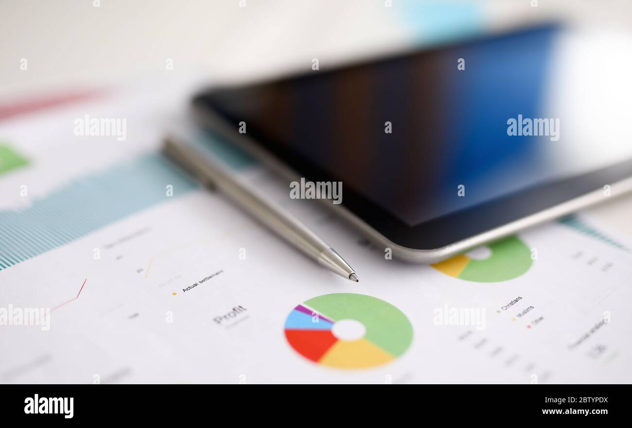 Silver pen adn digital tablet pc lie on office table against business chart background closeup Stock Photo