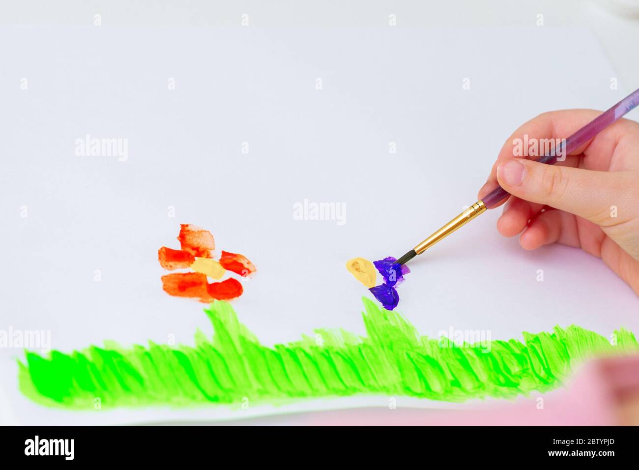 Child is drawing flowers by watercolors on white paper. Children's and Earth day concept. Stock Photo