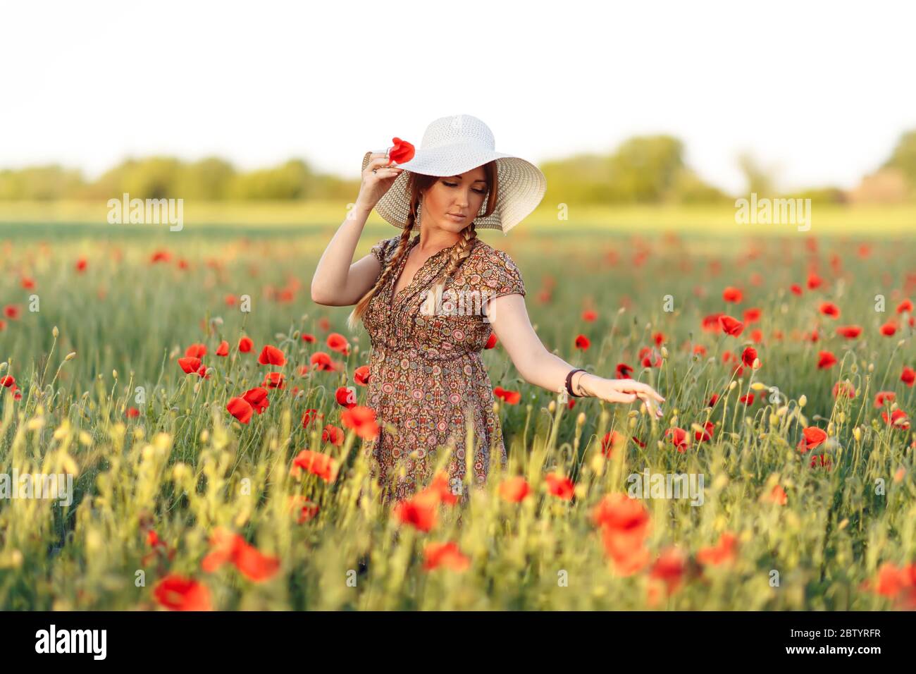 Beautiful redhead woman in white hat posing on green field with poppies ...