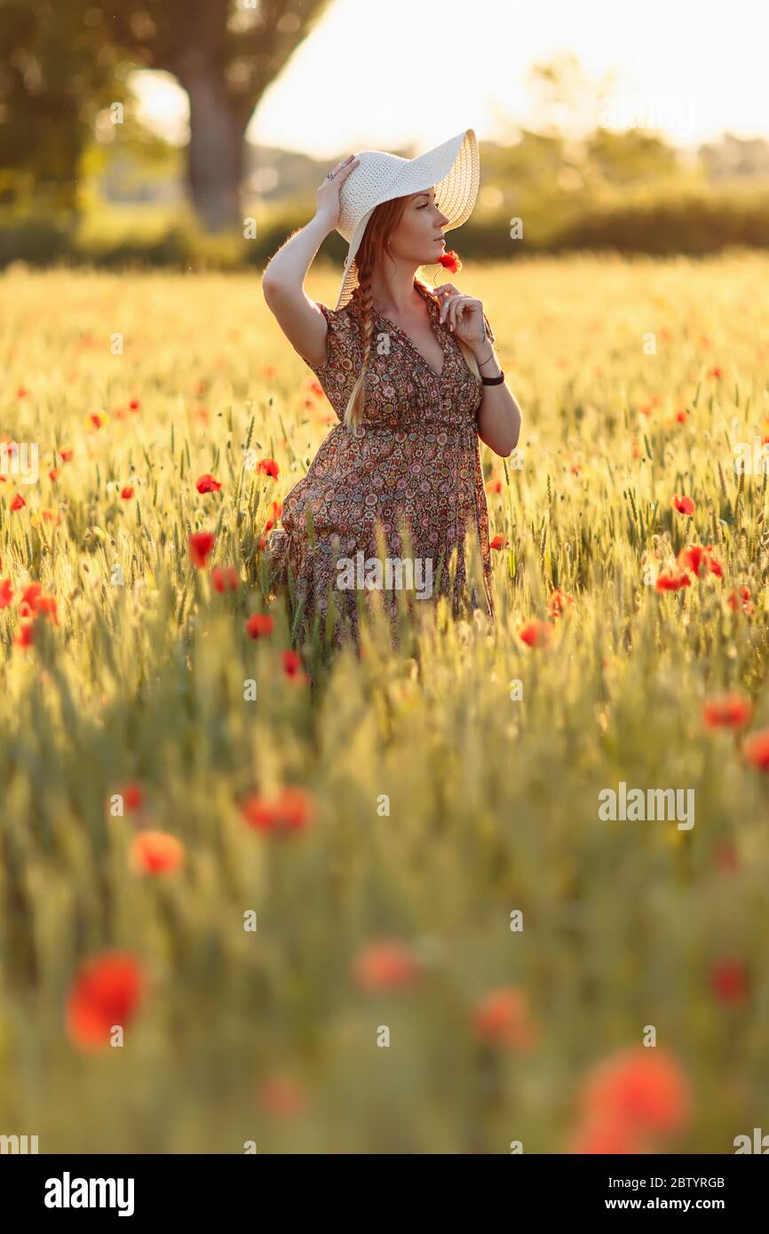Beautiful redhead woman in white hat posing on green field with poppies ...