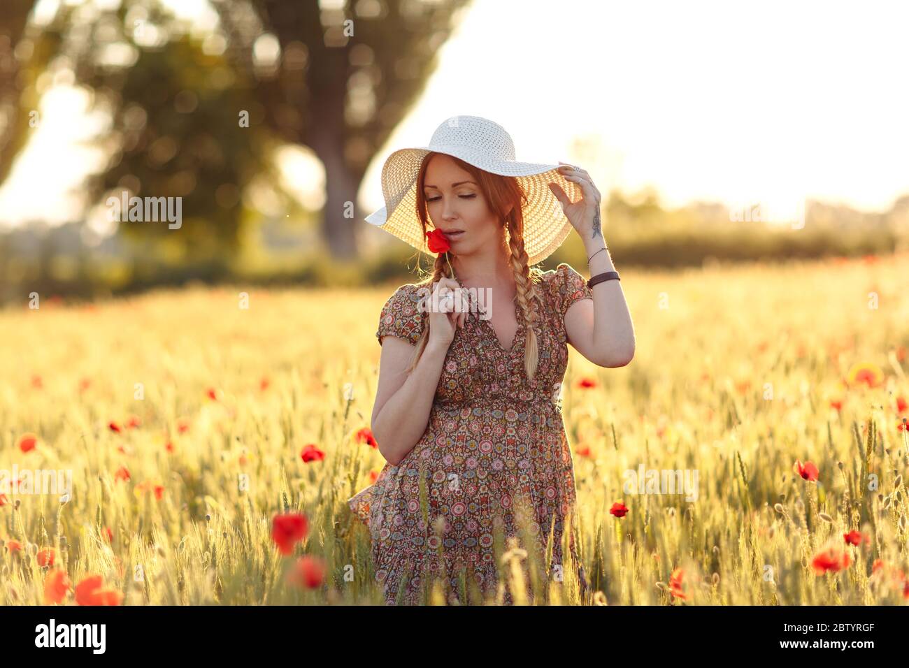 Beautiful redhead woman in white hat posing on green field with poppies ...