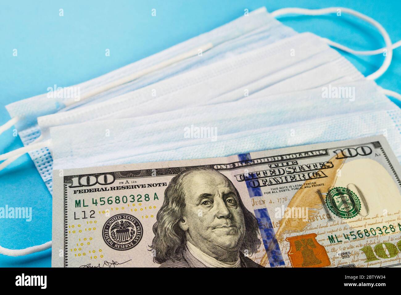 100 dollars banknote lie on medical masks on blue background. Concept of deficit, speculation and sold out of face masks. Selective focus Stock Photo