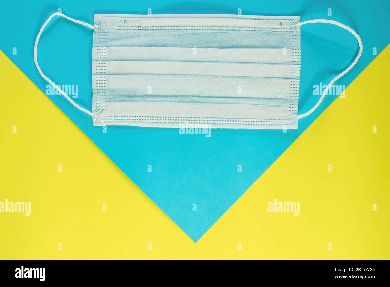 Face mask on blue and yellow background. Protection against coronavirus, allergies, flu. Medical mask, top view, copy space Stock Photo