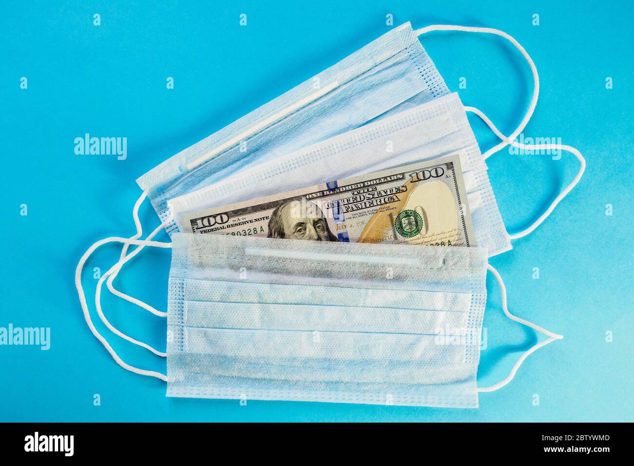 Face masks and banknote of 100 dollars on blue background. Concept of deficit, speculation and sold out of medical masks. Top view Stock Photo