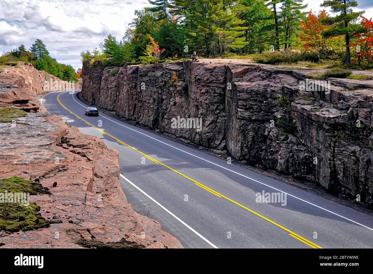 Milford Bay, Ontario / Canada - 10/05/2008: Mountain road cut through the pink granite rock. Landscape with rocks, autumn leaves color, and beautiful Stock Photo