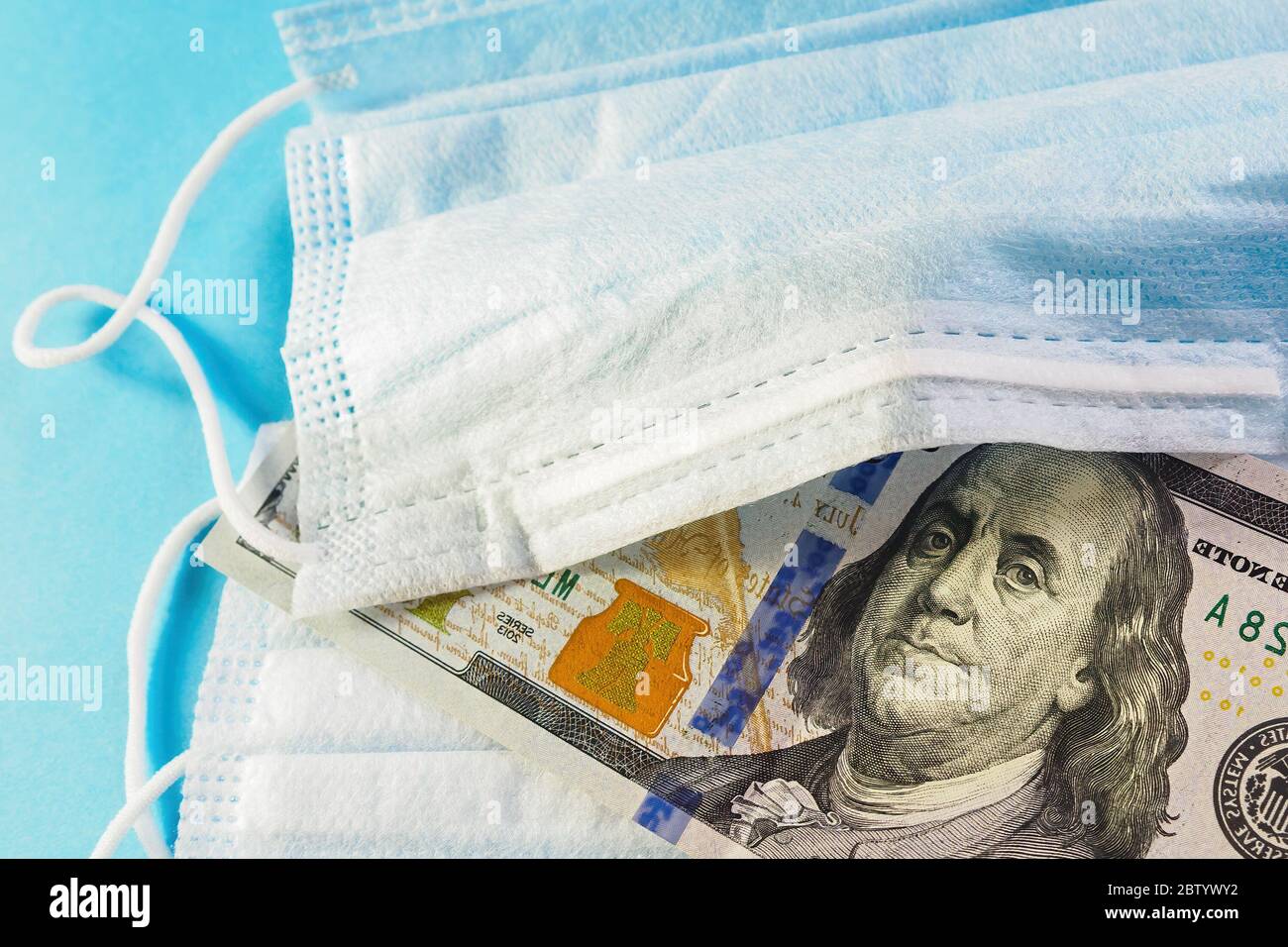 Face mask and banknote of 100 dollars on blue background. Concept of deficit, speculation and shortage of medical masks in sale. Selective focus, clos Stock Photo