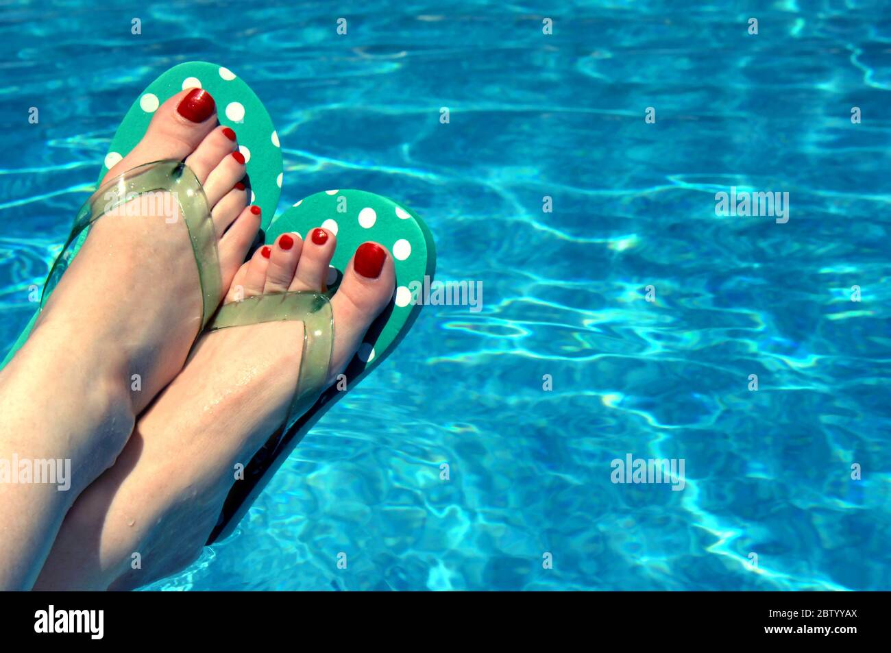 Aqua blue swimming pool frames polka-dotted flip flops worn by a woman with red  painted toe nails. Stock Photo