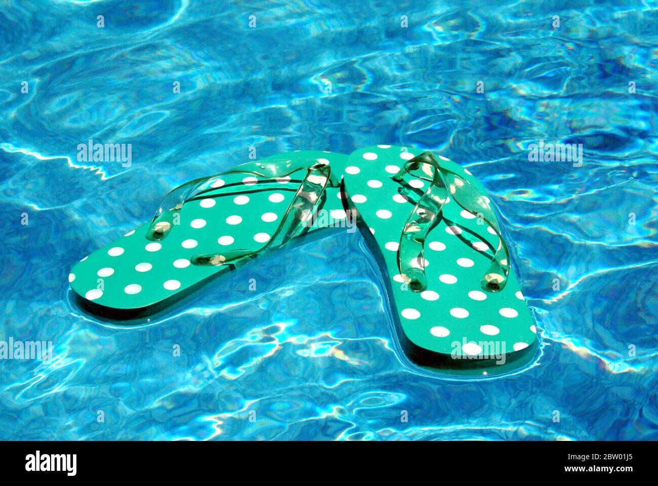 Turquoise polka-dotted flip flops float on the surface of a swimming pool. Stock Photo