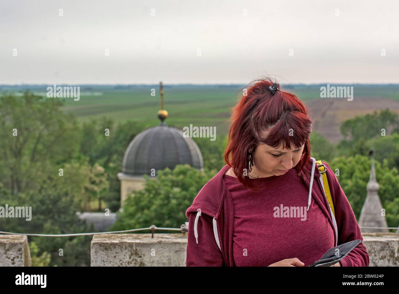 A young, beautiful woman had just received a message over the phone that she was reading at the top on the terrace of an old building. Stock Photo